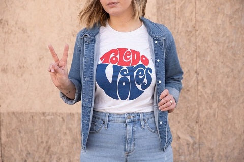 lady wearing denim jacket and pants in a “16153 Genova Votes” t-shirt